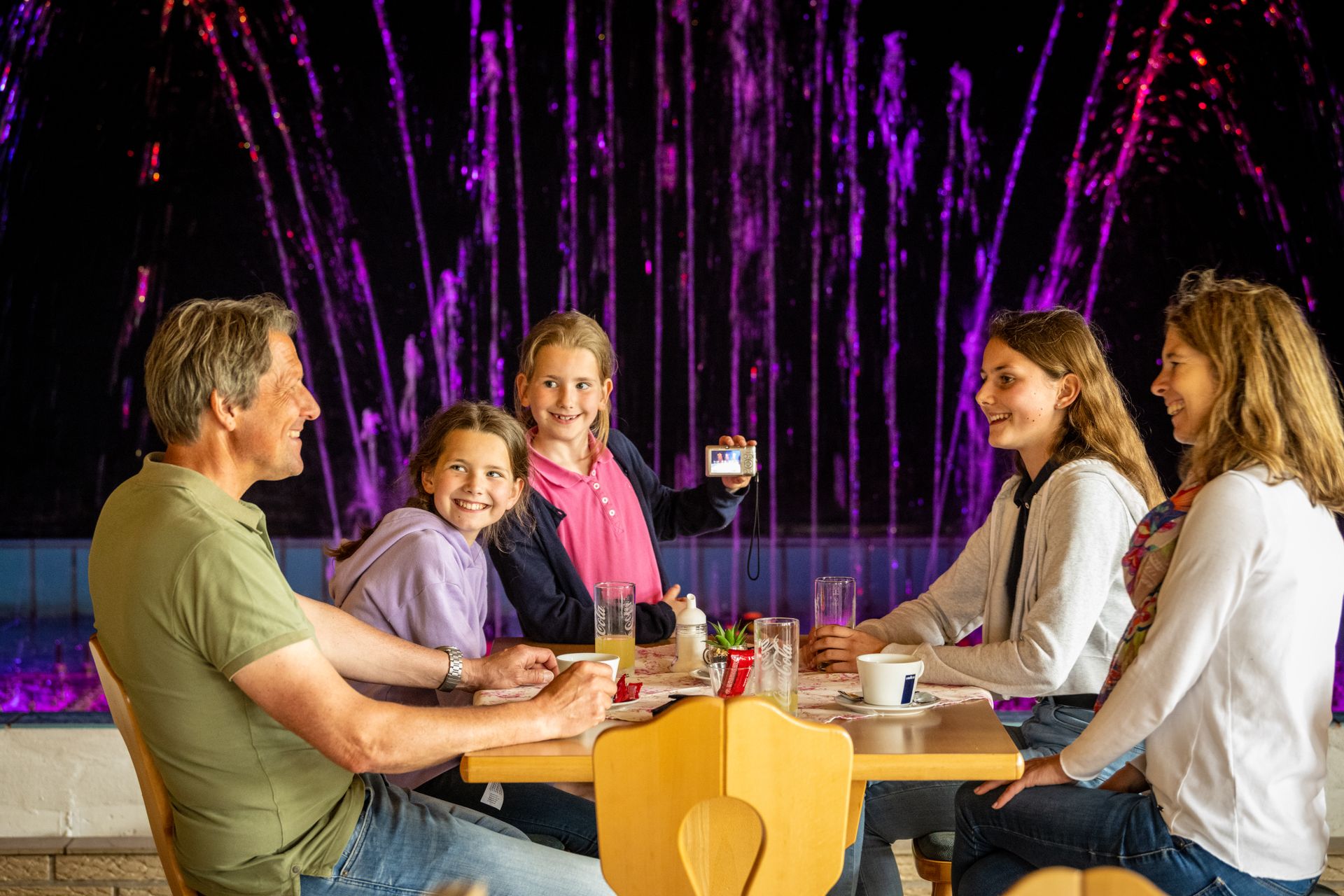 Eine Familie sitzt an einem Tisch und schaut auf die beleuchtete Wasserspielorgel.