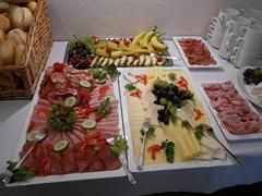Een buffet met verschillende vlees- en kaasplanken. Verse fruit zoals bananen en druiven zijn ook op de tafel gerangschikt.