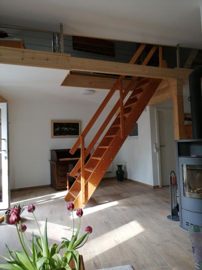 Een lichte kamer met een houten trap die naar de bovenverdieping leidt. Op de tafel staan tulpen, die voor een gezellige indruk zorgen.