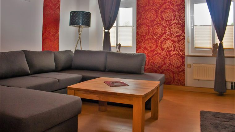 Ein stilvolles Wohnzimmer mit einem modernen grauen Sofa und einem Holzkaffee-Tisch. Die Wände sind rot dekoriert, und große Fenster lassen viel Licht hereinkommen.