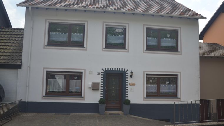 Een mooi, twee verdiepingen tellend woonhuis met witte muren en bruine ramen. De façade heeft een uitnodigende voordeur en grote ramen die veel licht binnenlaten.