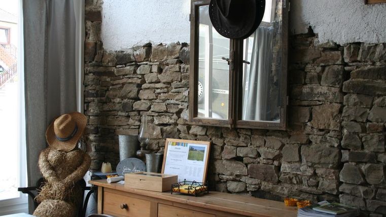 Een gezellige kamer met een stenen muur en een houten bureau. Op de achtergrond bevindt zich een spiegel en een foto, evenals een ronde hoed aan de muur.