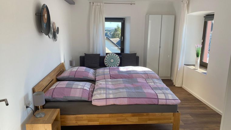 Ein gemütliches Schlafzimmer mit einem großen Bett und Holzfußboden. Die Wände sind hell, und es gibt Fenster, die viel Licht hineinlassen.