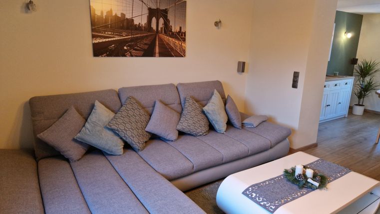 Ein modernes Wohnzimmer mit einem grauen Sofa und vielen Kissen. An der Wand hängt ein Bild der Brooklyn Bridge, und ein eleganter Couchtisch ziert den Raum.
