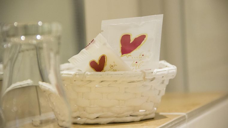 Ein weißer Korb mit Papiertüchern, auf denen rote Herzen gemalt sind. Der Korb steht auf einem Holzregal.