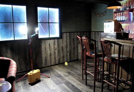 Dimly lit room with bar and bar stools, taped-up window and sofa area.