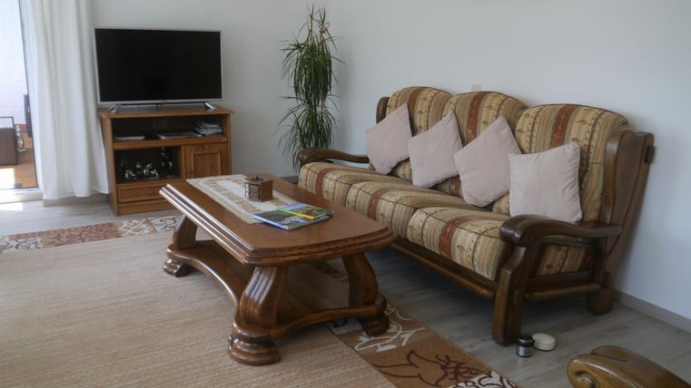 Ein gemütliches Wohnzimmer mit einem bequemen Sofa und einem Holztisch. Ein Fernseher und eine Pflanze ergänzen die Einrichtung.