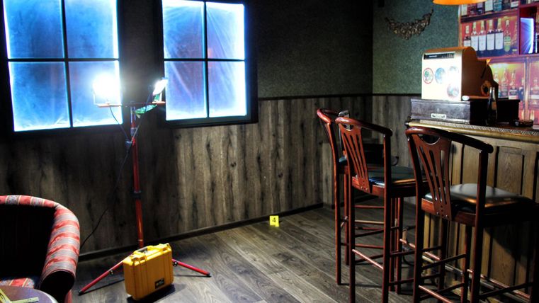 Une pièce confortable avec un bar et des tabourets. Deux fenêtres laissent entrer la lumière, tandis qu'une lampe et un appareil jaune se trouvent dans la pièce.