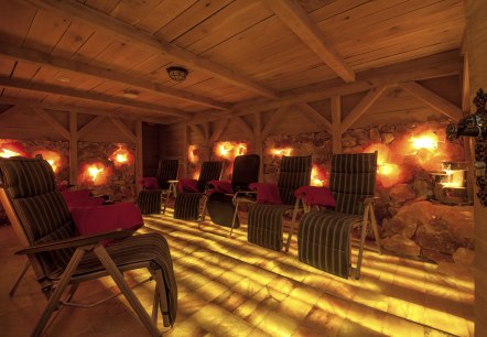 A dark room with a wooden ceiling and walls made of salt stones. There are several loungers in the room.
