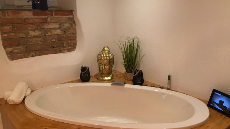 Une salle de bain moderne avec une baignoire ovale en bois. À côté de la baignoire se trouvent une statue de Bouddha et quelques éléments décoratifs.