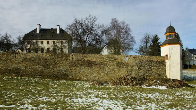 Schloss Oberehe mit einer alten Steinmauer und einem kleinen Turm im Vordergrund. Der Boden ist teilweise mit Schnee bedeckt, Bäume ohne Blätter.
