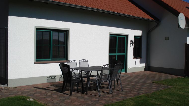 Een modern huis met een verzorgde buitenruimte. Voor het huis staat een ronde tafel met stoelen op een bestratingtapijt.