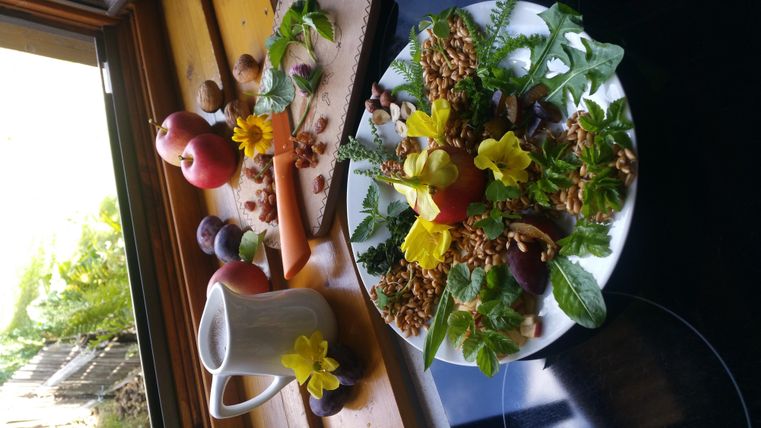 A beautiful fruit and salad platter with fresh ingredients and edible flowers. Next to the platter are apples, nuts, and a small coffee pot.